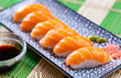 Against background of wooden table is rectangular plate of maki sushi set with nigari rolls, complemented with wasabi