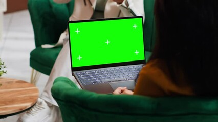 Hotel guest using laptop with greenscreen layout in lobby, looking at copyspace chromakey display in lounge area. Modern person holding pc showing isolated mockup template on screen.