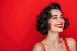 © Melanthe - Curly brunette young woman with red lipstick smiling. Pinup girl with stylish haircut and bright makeup on red background. Fashion, beauty and Women's Day concept. Retro, 90s style