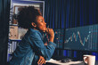Young African woman trader smiling on happy face, looking on screen with valued stock market chart at high profit. Concept of exchange investment online in trading application on pc. Tastemaker.