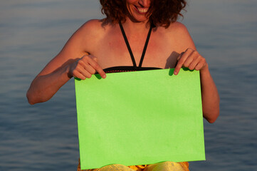 Mid Adult Woman in Swimsuit and Straw Hat on a Beach holding over Breasts a Green Screen Canvas - Copy Space Female Vacation Concept