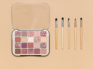 Wall Mural - Stacked makeup brushes and a set of eye shadow on a beige background.