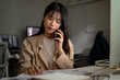 © bongkarn - A professional Asian businessman is having a serious phone call, working at her desk in the office.