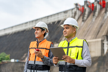 Wall Mural - Confident asian two maintenance engineers man inspection discussstion with tablet at construction site dam with hydroelectric power plant and irrigation. Team engineer man working at project