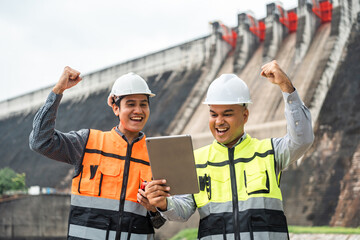 Wall Mural - Confident asian two maintenance engineers man inspection discussstion with tablet at construction site dam with hydroelectric power plant and irrigation. Team engineer man working at project