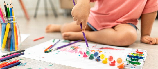 Happy moment little cute girl creating and water color painting activity with paint brushes on frame canvas at living room. Kids activity. Child physical, Emotional, Cognitive development concept.