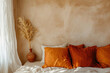 A cozy boho-style bedroom featuring rustic terracotta vase with pampas grass, burnt orange pillows, and a creamy textured wall