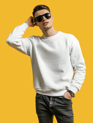 Wall Mural - Portrait of handsome man with sunglasses wearing white Sweatshirt and dark grey jeans with short hairstyle cut isolated on yellow background