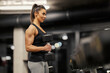 © dusanpetkovic1 - A strong muscular woman is standing in a gym and doing workouts for biceps.