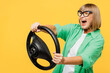 Side view surprised shocked elderly blonde woman 50s years old wears green shirt glasses casual clothes hold steering wheel driving car isolated on plain yellow background studio. Lifestyle concept.