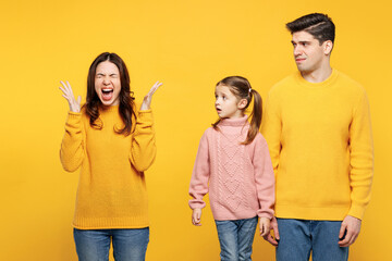 Wall Mural - Young sad mad unhappy parents mom dad with child kid girl 7-8 years old wear pink knitted sweater casual clothes spread hands scream be stressed isolated on plain yellow background Family day concept