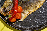 Fototapeta  - Fried sea bass with baked tomatoes in a black plate on a yellow background