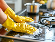 Person cleaning a gas stove top with yellow rubber gloves. Housekeeping and kitchen maintenance concept with copy space for design and print