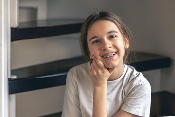 a teenage girl with braces smiles at home, showing her teeth.