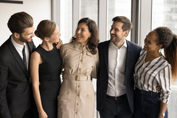 Poster - Happy successful diverse colleagues standing close together, hugging, talking, laughing. Multiethnic business team and mature female leader enjoying teamwork success, discussing good job results