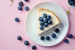 Plain New York cheesecake with blueberries on a white plate viewed from the top against a pink background
