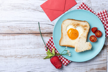 Wall Mural - Valentine's Day breakfast with egg with tomatoes, heart shaped and toast bread on wooden table. Top view. Copy space