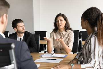 Wall Mural - Mature businesswoman talking to multiethnic colleagues at meeting table, sharing management strategy vision, explaining idea for marketing, brainstorming on startup project with business group