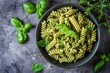Top view of Italian cuisine fusili pasta with basil pesto herbs on a gray stone background