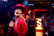© luengo_ua - Joy and music. Happy young woman in red hat is singing in karaoke nightclub