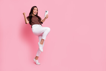 Wall Mural - Full length photo of addicted casino play young woman loves gambling using smartphone raised fist up isolated on pink color background