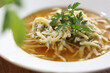 Broth with homemade noodles, sprinkled with parsley, in a white bowl. Lunch at a restaurant, soup, close up.