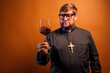 © karrastock - Portrait of a priest with crucifix and sunglasses drinking wine.
