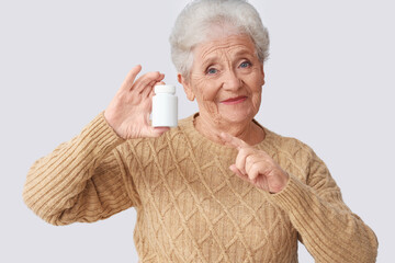 Sticker - Senior woman pointing at pill bottle on light background