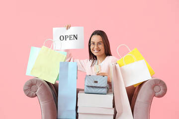 Sticker - Female seller with OPEN sign and shopping bags in armchair on pink background