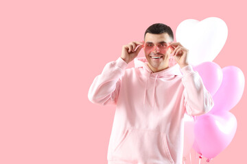 Poster - Handsome man in heart-shaped sunglasses and balloons on pink background. Valentine's Day celebration