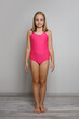 © millaf - Young girl child wearing pink swimsuit standing on white studio wall background