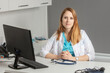 © nick_fedirko - Portrait of young female medicine doctor sitting and working at her office. Healthcare and medical concept.Doctor in white coat doing paperwork at workplace with laptop, writing notes in the clinic.