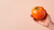 Hand holding persimmon fruit isolated on pastel background
