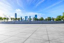 Empty Square Floor And Green Palm Trees With City Skyline Under Blue Sky