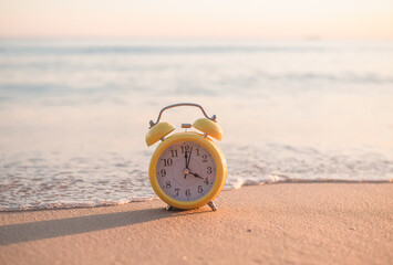 Yellow alarm clock on the beach in the sunset time. The concept about Time to summer, Travel, Vacation and Relaxation