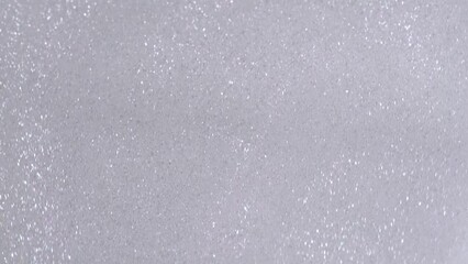 Wall Mural - Silver glitter cosmetic product flow down on white background. Liquid drops of lotion with shimmer pouring flow down on canvas. Shiny silver shimmer paint dripping on the white wall