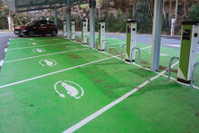 A Row Of Electric Vehicle Charging Stations Marked By Green Paint On The Pavement With A Solar Panel Roof Overhead
