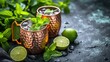  two copper mugs filled with ice, mint, and lime on top of a table with mint and limes.