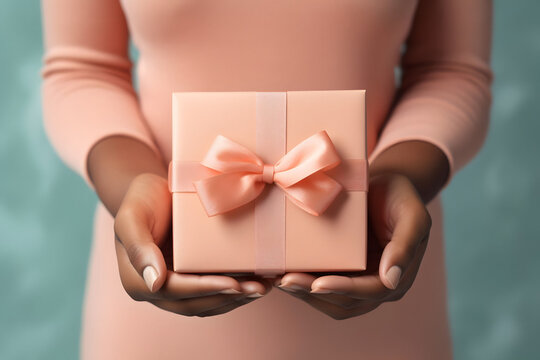 Close-up of black woman's hands holding a small gift wrapped in peach ribbon