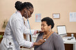 © Seventyfour - Young African American physician using stethoscope while asking senior female patient to make a deep breath during medical examination