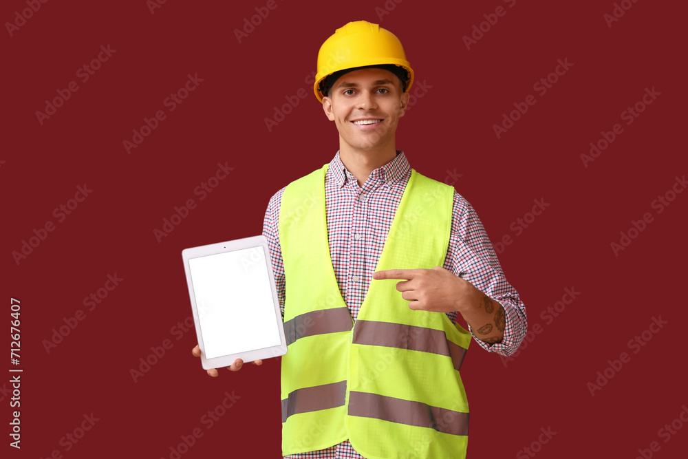 Young male engineer pointing at tablet computer with blank screen on red background
