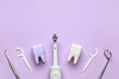 Plastic tooth models, electric toothbrush, floss toothpicks and dental tools on lilac background. World Dentist Day