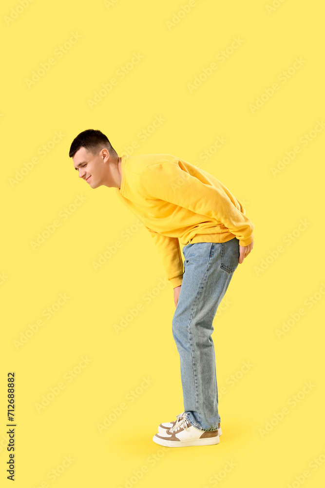 Young man with hemorrhoids on yellow background