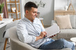 © Pixel-Shot - Young man reading book in armchair at home