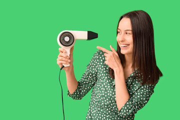 Sticker - Beautiful young woman pointing at hair dryer on green background