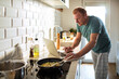 © Marko Geber - Middle aged man cooking and using a laptop at home in the kitchen