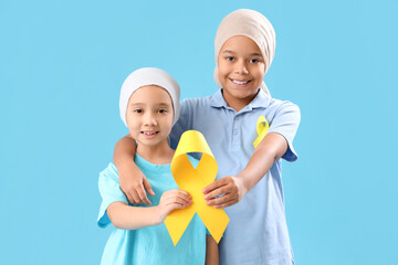 Wall Mural - Cute little children after chemotherapy with yellow ribbons on blue background. Childhood cancer awareness concept