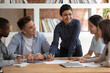 Smiling multiracial diverse students sit ta desk in classroom studying together discuss paperwork project, happy multiethnic young people involved in team activity at lesson in class, teamwork concept