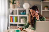 Fototapeta  - Businesswoman working at home while talking on a phone and taking notes