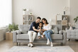 © fizkes - Positive young mom, dad and sweet girl kid taking family selfie on cozy comfortable couch, having fun with digital gadget in cozy stylish home interior, using smartphone for selfie together